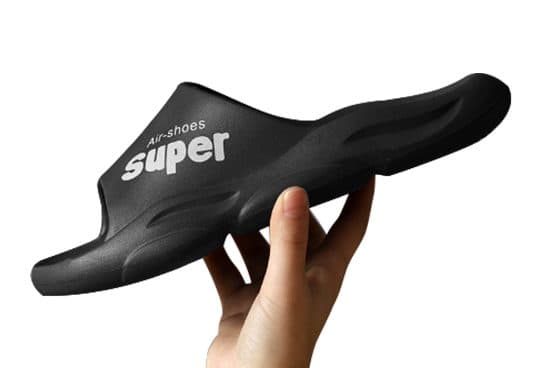Hand holding a black AirFlops slide sideways to show the thick ridged sole and the strap printed Super Air-shoes
