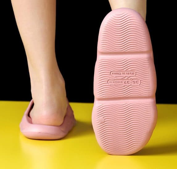 Pink AirFlops sole with a wavy tread and a 36-37 size mark, next to a foot wearing the other slide on a yellow floor