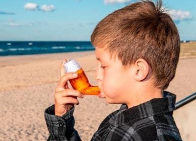 A boy at the beach breathing out through the AirPhysio for Children device