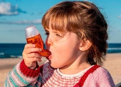 A young girl in a knitted jumper holding the AirPhysio for Children to her mouth