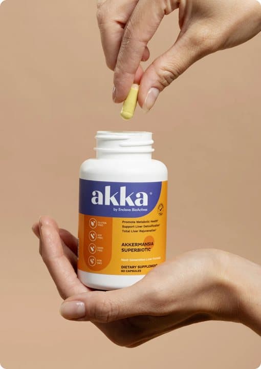 A hand holding an open Akka bottle while another hand drops in a yellow capsule