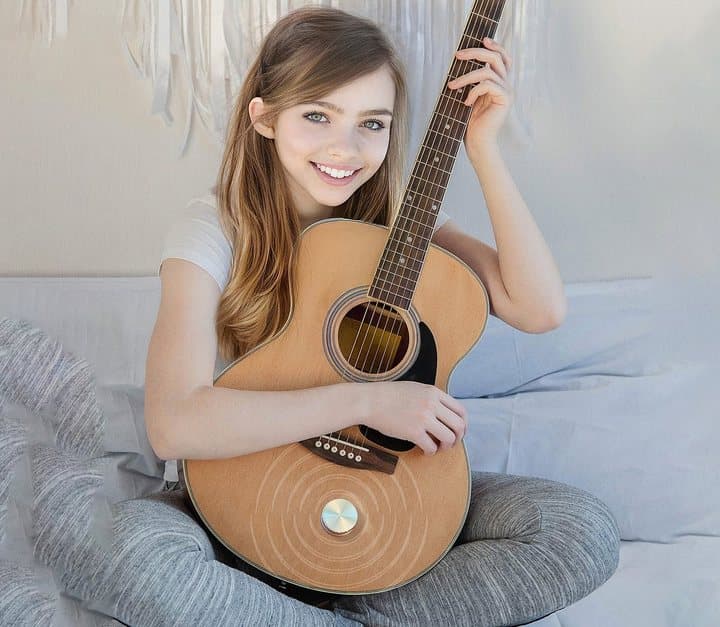 Young woman holding an acoustic guitar with an Anything Speaker attached to its body