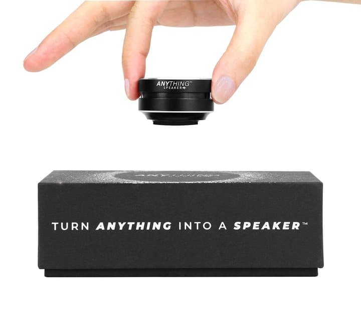 Fingers holding the small round Anything Speaker above its black presentation box