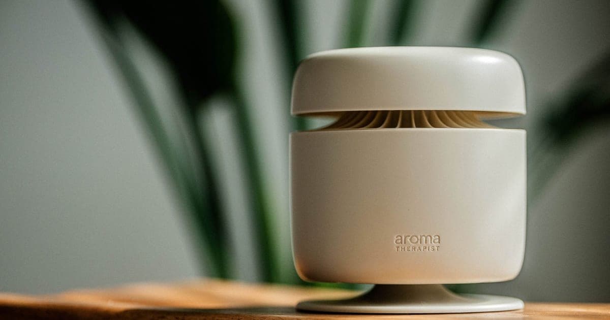 Beige Aroma Amplifier diffuser on a wooden side table with a plant behind it