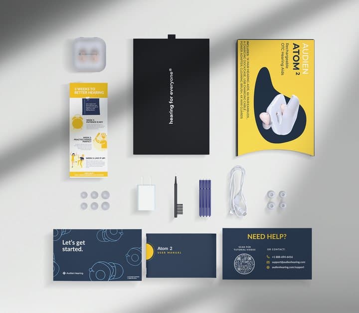 Flat lay of Audien box contents including case, tips, charger, brush and an Atom 2 user manual