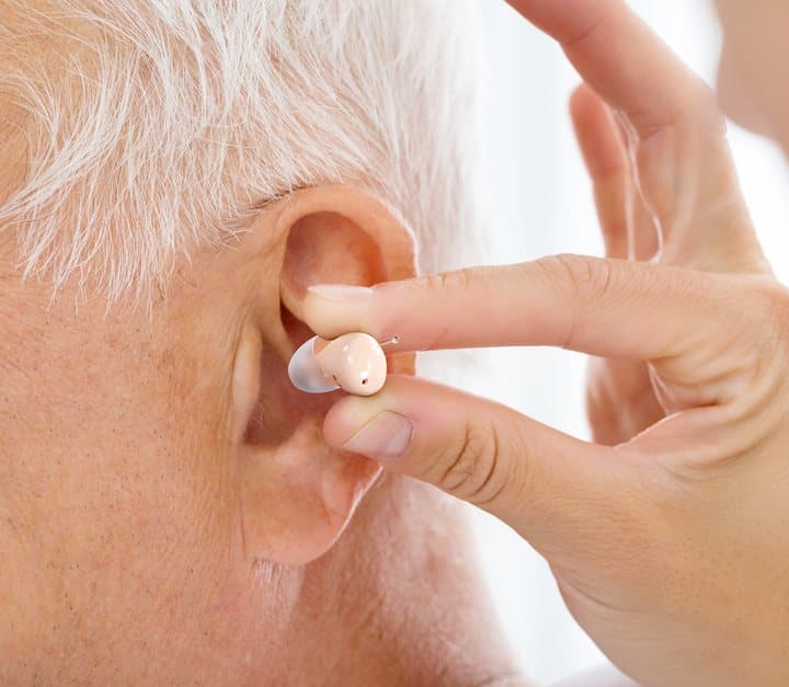 Close-up of fingers placing a small beige Audien hearing aid into an older man's ear