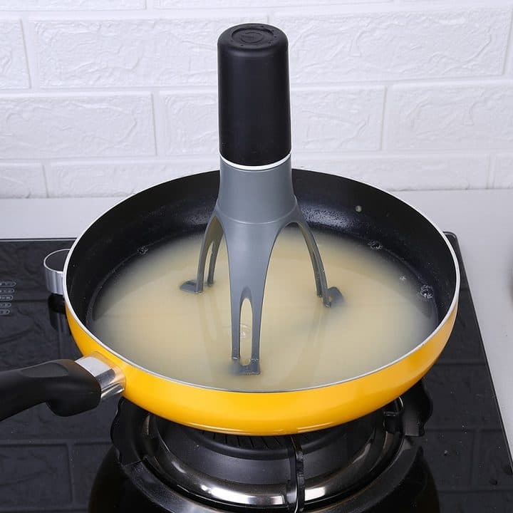 AutoMix standing in a yellow pan of liquid on a black gas hob against a white brick wall