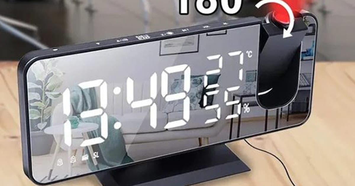 Black BigTime Pro mirror clock showing 13:49 in large white digits with 27 degrees and 55 percent humidity, its red projector rotating to show the time on a wall