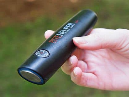 A hand holding a black pen labelled BiteHelper with a round metal tip, outdoors, used for the stainless steel tip add-on