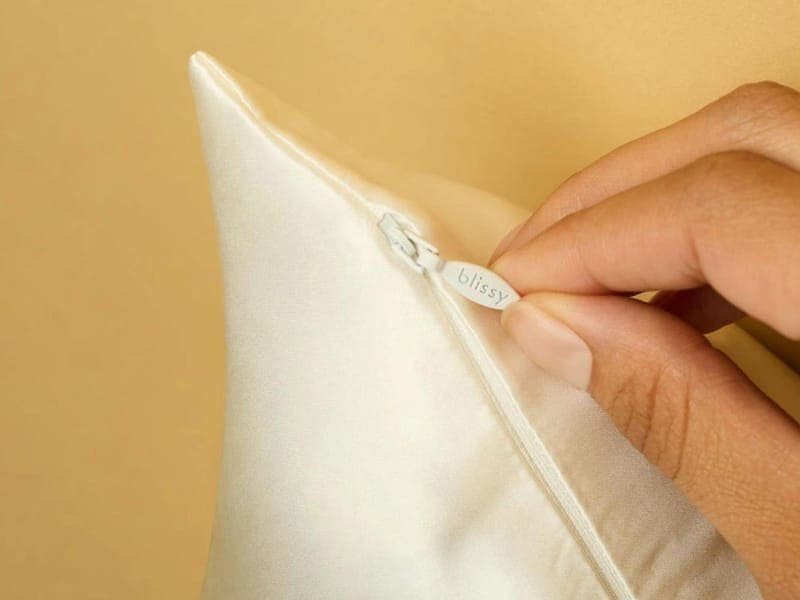 Hand opening the hidden zipper along the short edge of a white Blissy silk pillowcase