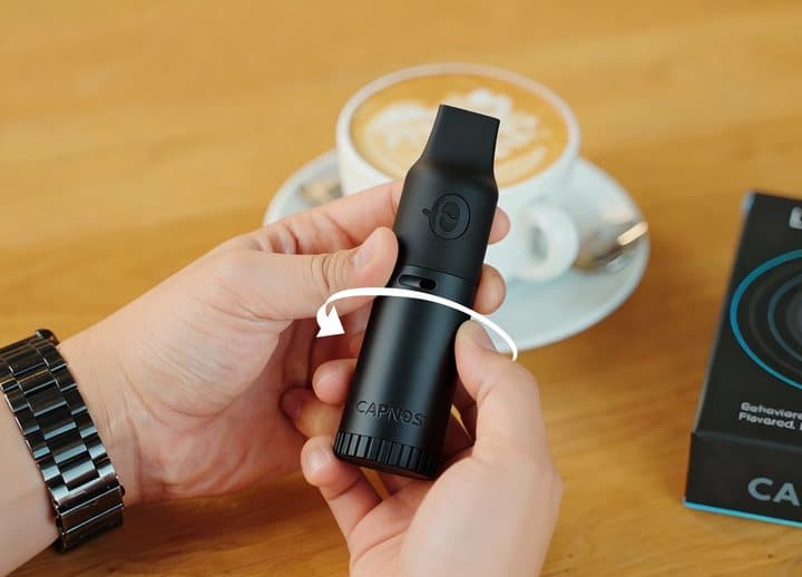 Hands twisting the top of the Capnos Legura to adjust the airflow beside a coffee cup