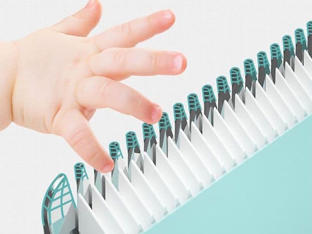 Small child's hand touching rounded white and teal clipper comb teeth in close-up