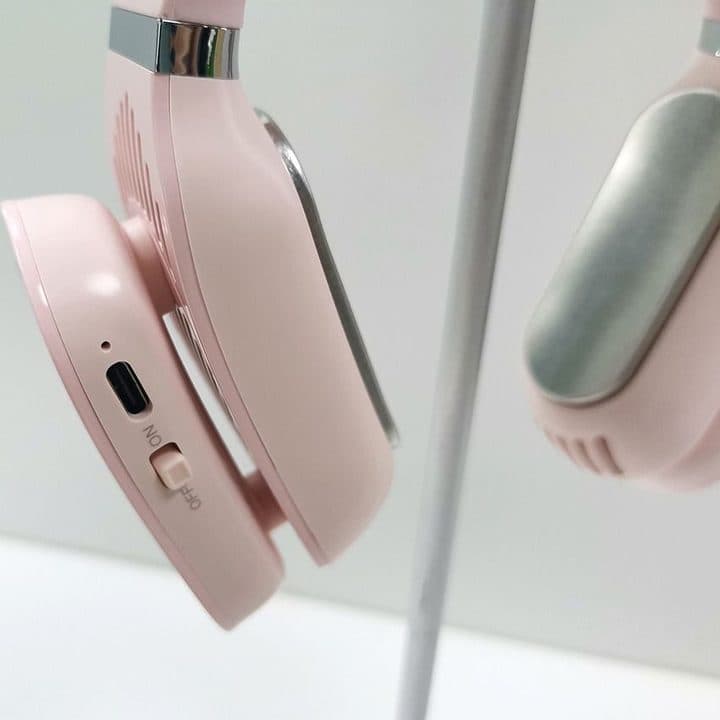 Pink version of the neck device hanging on a stand, showing a USB-C port, an on-off switch and a metal plate