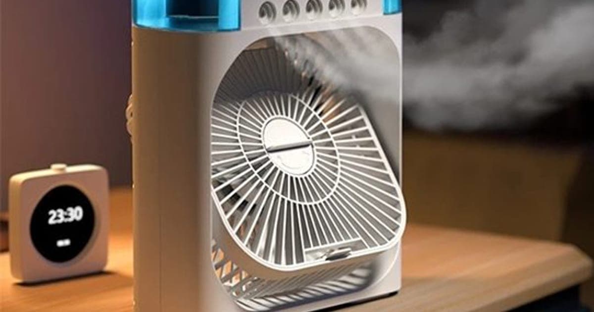 White CoolTime box fan with a blue-lit clear top tank, a brown carry strap and mist spraying from above the round grille, beside a bedside clock