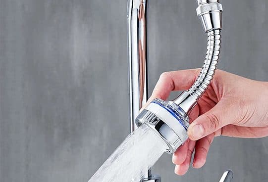 Chrome FaucetMaster flexible tap extender screwed onto a tap, held by a hand with water spraying from the head