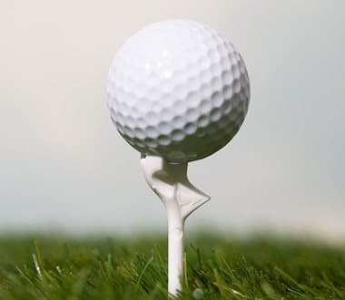 Golf ball resting on the angled head of a white FlightPath tee on a course