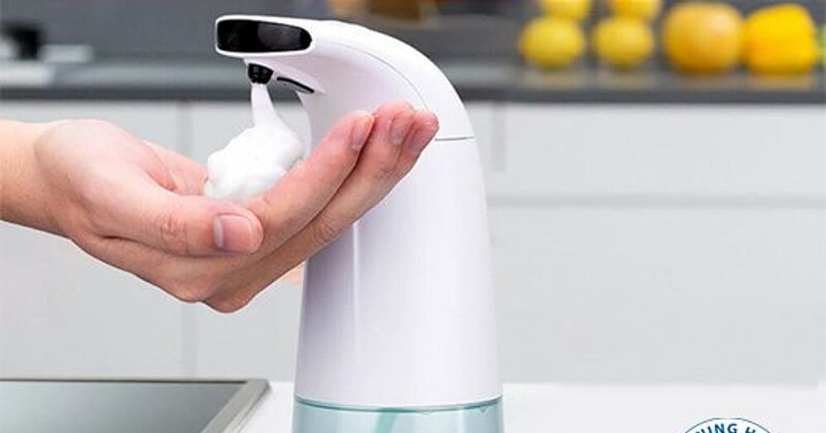 White Foamatic sensor dispenser on a kitchen counter dropping foam into a hand, with green soap in its clear tank