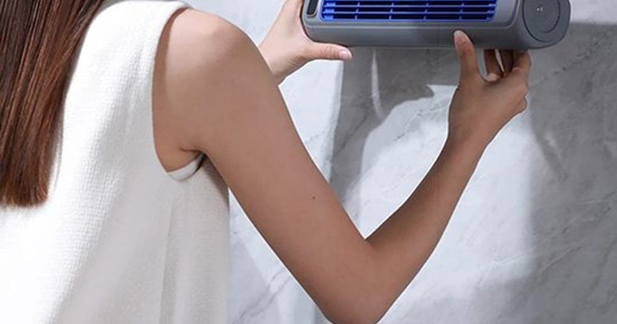Woman hanging a grey FreshAir Pro tube fan with a blue grille on a hook on a marble wall