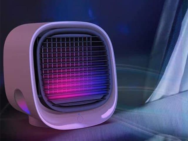 FreshBreeze cooler glowing pink and purple behind its grille in a dark room next to a curtain