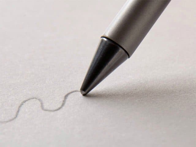 Close-up of a silver metal pen tip drawing a thin grey wavy line on paper