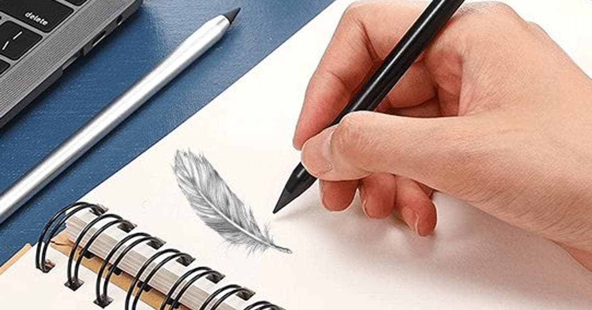 Hand writing with a black FutureX Pen in a spiral notebook beside a grey pencil-like sketch of a feather, with a silver pen and laptop behind