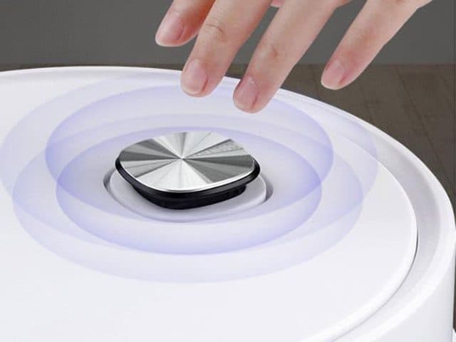 Finger about to press the silver one-touch button on top of the white GoClean Robot, with ripple graphics