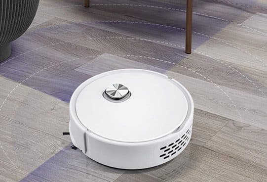 White GoClean Robot vacuum with side vents and a silver button on a wooden floor near a chair leg and a grey pot