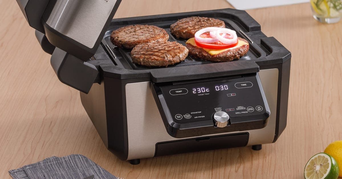 Gourmax Pro open on a wooden counter with burger patties cooking on the griddle plate
