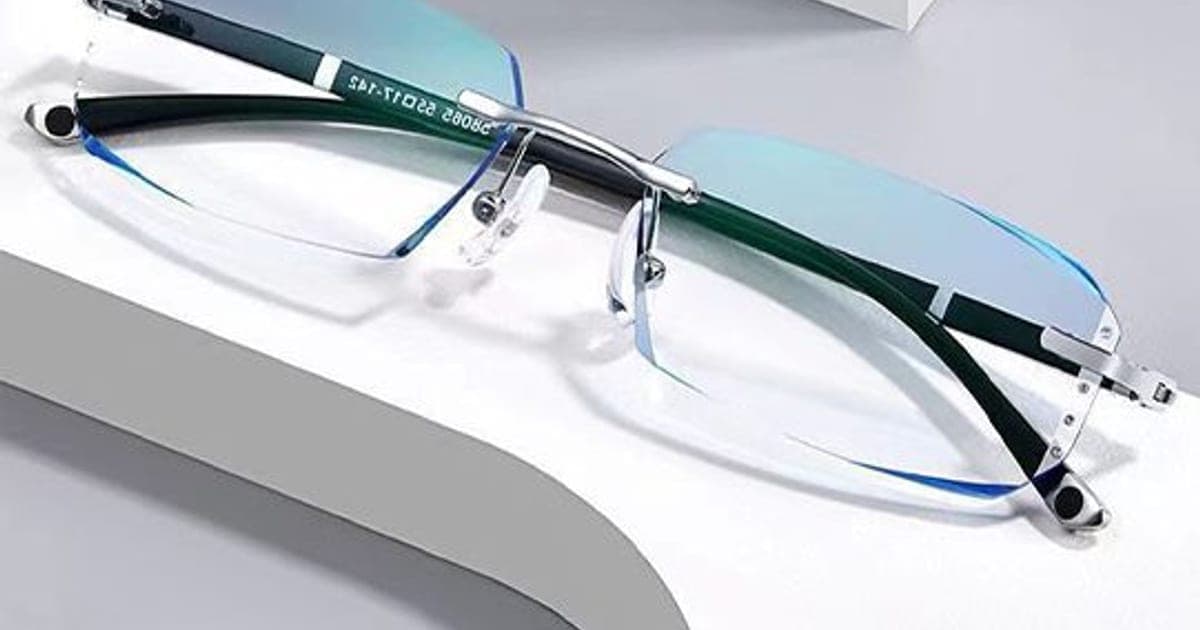 Rimless GuardBlue Vision glasses with silver hinges and dark arms resting on a white surface, the lenses showing a blue-green reflective tint