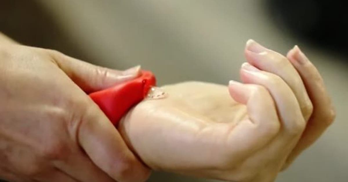 A hand squeezing a red Handsan Wrist silicone band to dispense clear sanitizer into the palm
