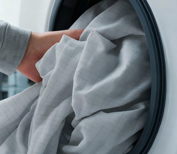 Hand placing a grey Heal Naturally grounding sheet with its silver grid into a front-loading washing machine
