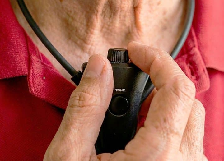 Close-up of a hand adjusting the volume on the HearDirect receiver hanging under the wearer's chin