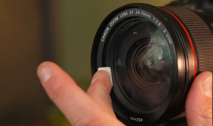 Fingertip with a small Jiffys pad wiping the front of a camera zoom lens