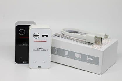 Black and white laser projection keyboard units standing on a white box beside a flat white micro USB cable