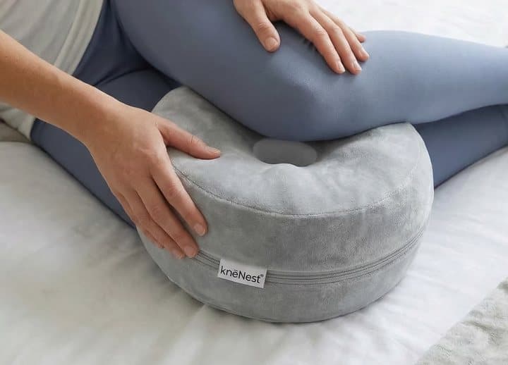 Person placing the knēNest pillow between the knees while lying on a bed