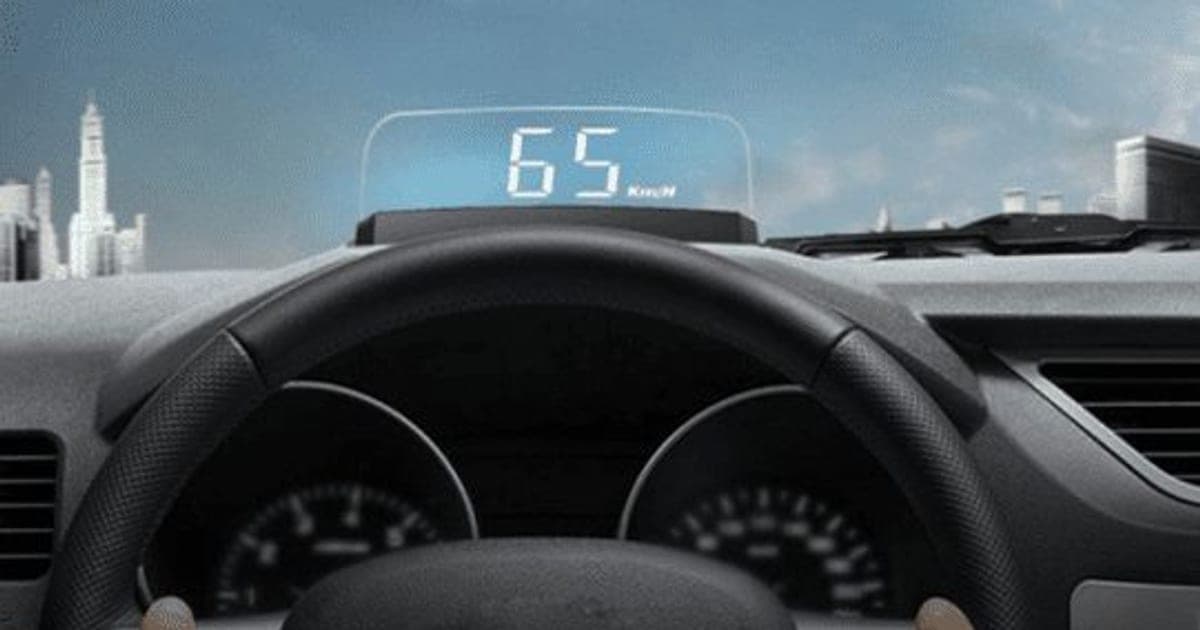 Driver's view of a steering wheel and dashboard with a MasterHUD Pro display showing 65 km/h reflected at the base of the windscreen