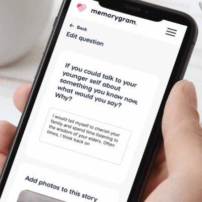 Hand holding a phone showing a Memorygram question being edited with an option to add photos