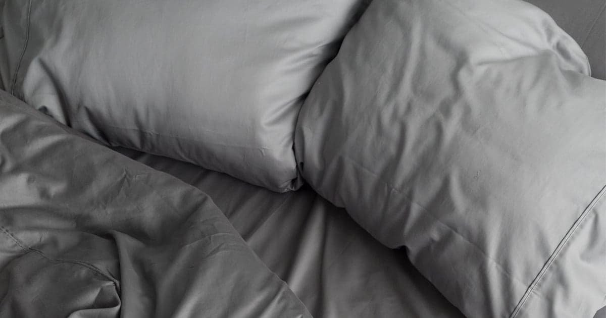 Two stone grey Miracle Made pillowcases on pillows on a bed made with matching grey sheets