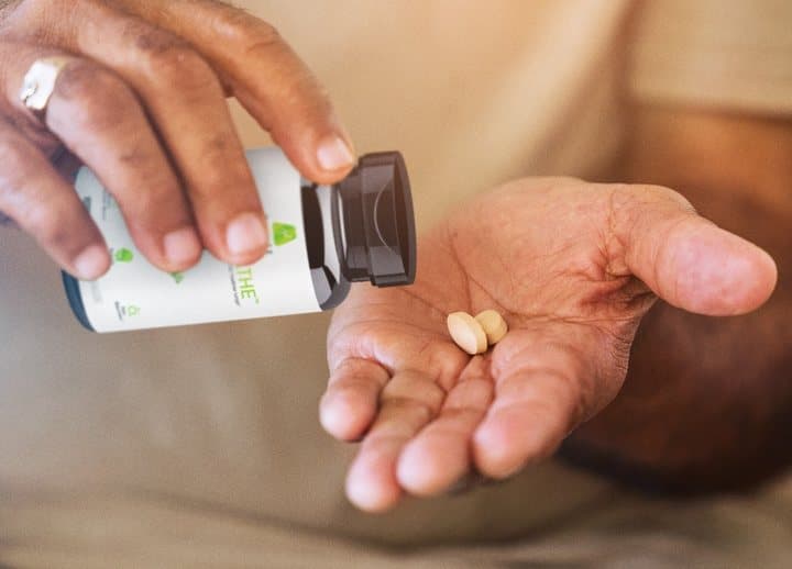 Hand pouring two OmniBreathe capsules from the bottle into a palm
