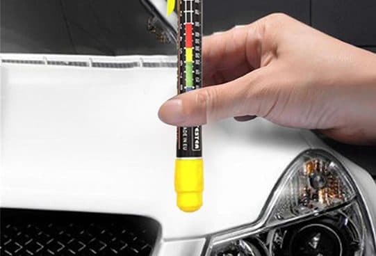 PaintPen Pro pen gauge with a black body, coloured scale and yellow magnetic tip held against the front of a white car near the headlight
