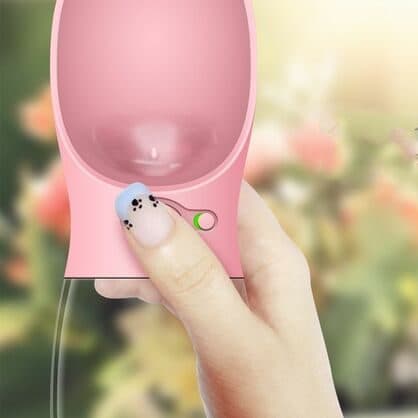 Hand holding a pink PetHydro Max with a thumb on the paw-print button and a small slide lock beside it