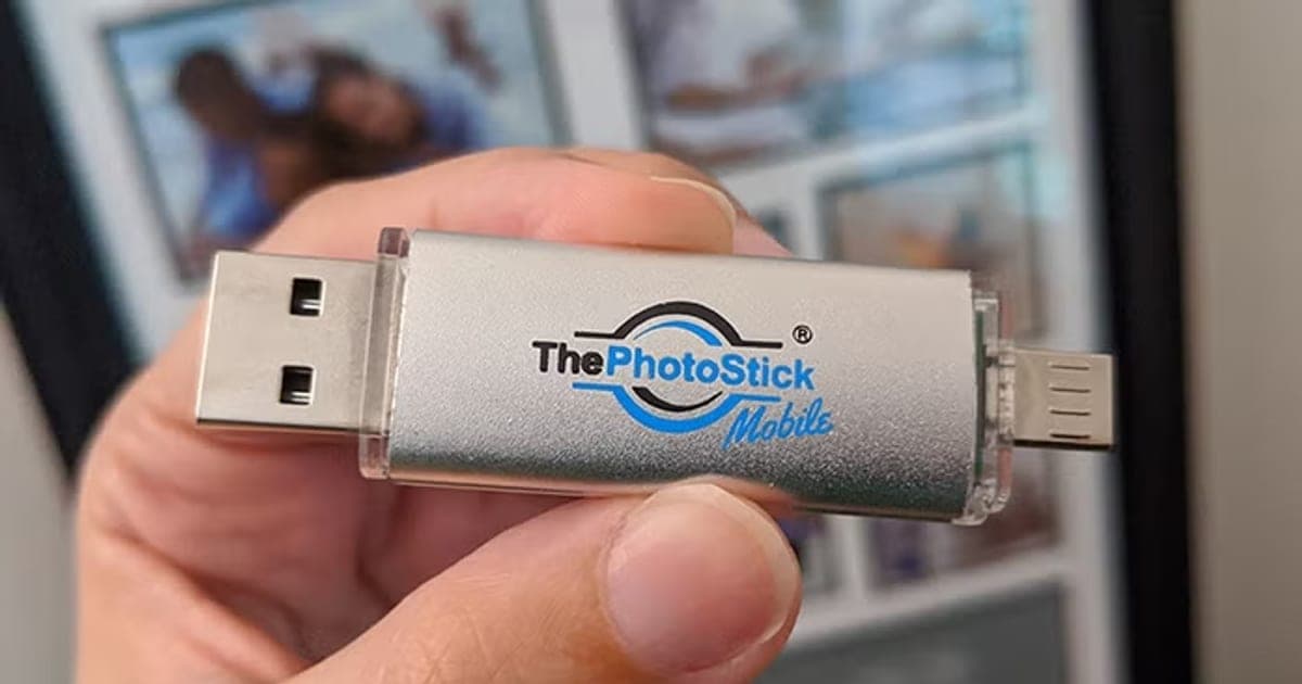 Hand holding a silver ThePhotoStick Mobile with a USB plug at one end and a phone connector at the other