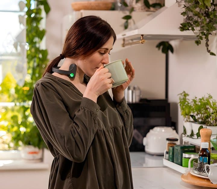 Woman drinking from a mug in her kitchen while wearing the Pulsetto neckband