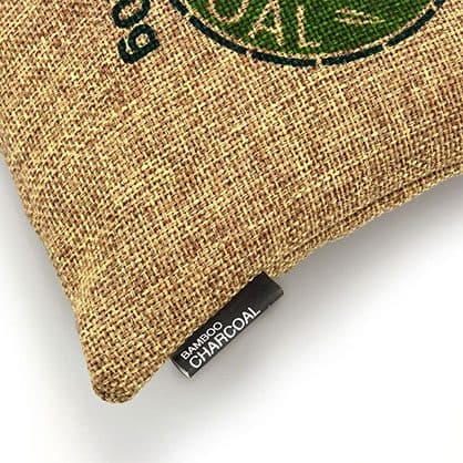 Close-up of a tan linen charcoal bag with a printed green logo and a black bamboo charcoal tag, used for the performance bag add-on