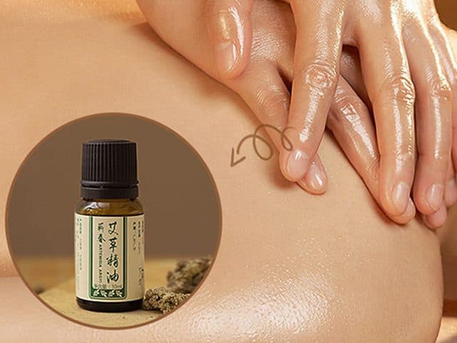 Small amber bottle of mugwort essential oil with a Chinese label in front of hands massaging oiled skin