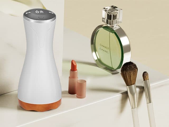 RelaxMe Pro massager standing upright on a white dressing table next to a lipstick, make-up brushes and a green perfume bottle