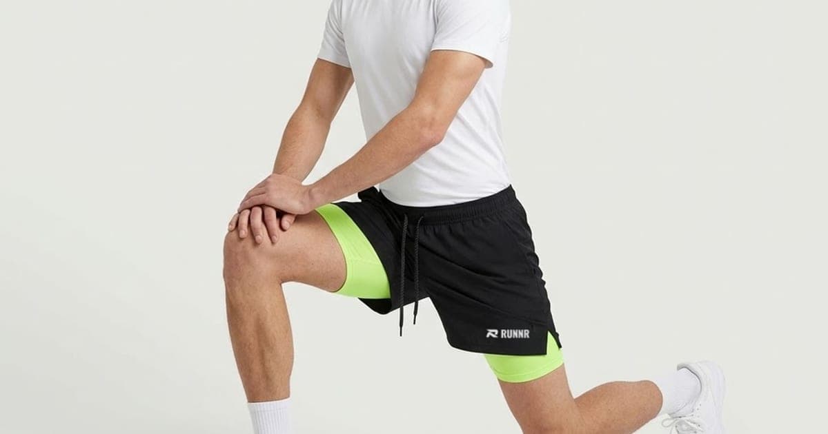 Man in a white T-shirt and black RUNNR 2-in-1 running shorts with a lime liner, stretching in a lunge