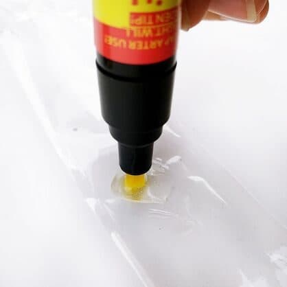 ScratchUndo Pro pen pressed onto clear plastic film, with a pool of clear liquid around the yellow tip