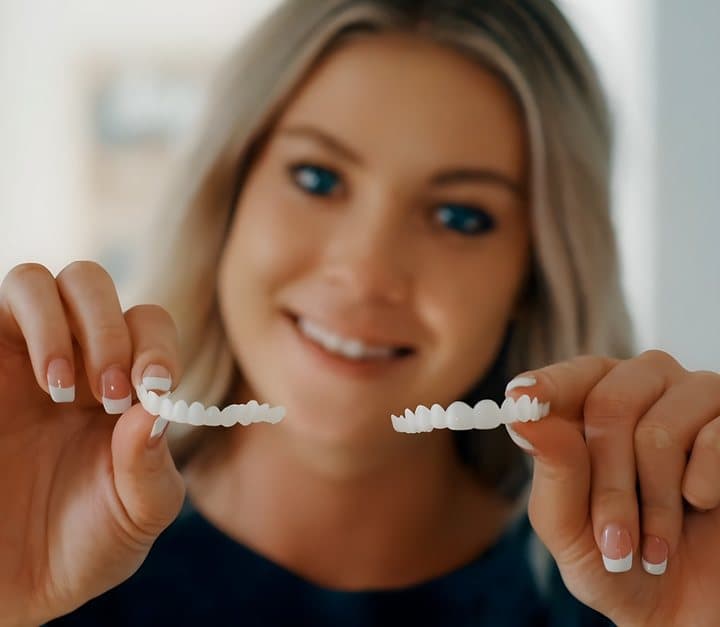 Woman holding a pair of Shiny Smile veneers in front of her smile