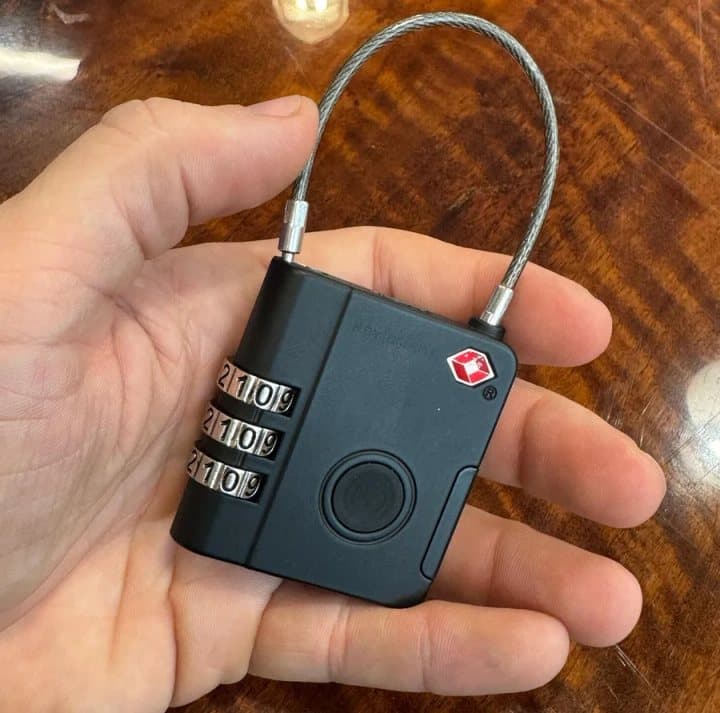 Hand holding the black KeySmart SmartLock showing its three dials, round button and red Travel Sentry diamond